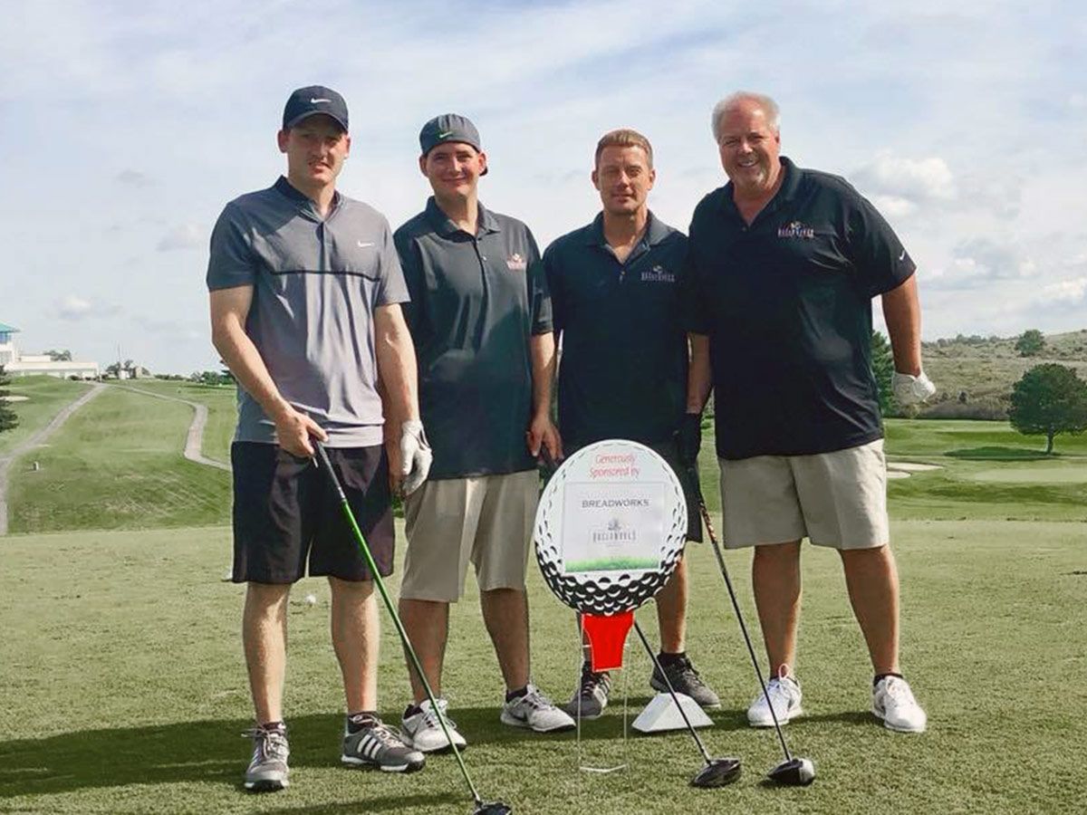 A golf foursome beside a hole sponsor sign at the GPHA golf outing